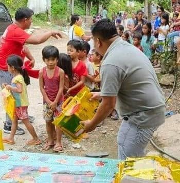 A volunteer preparing food packs for children waiting nearby